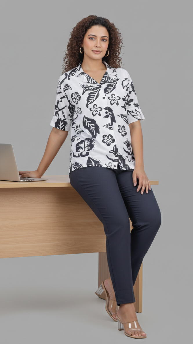 Woman sitting at a desk with a laptop, wearing a floral blouse and dark pants on a gray background