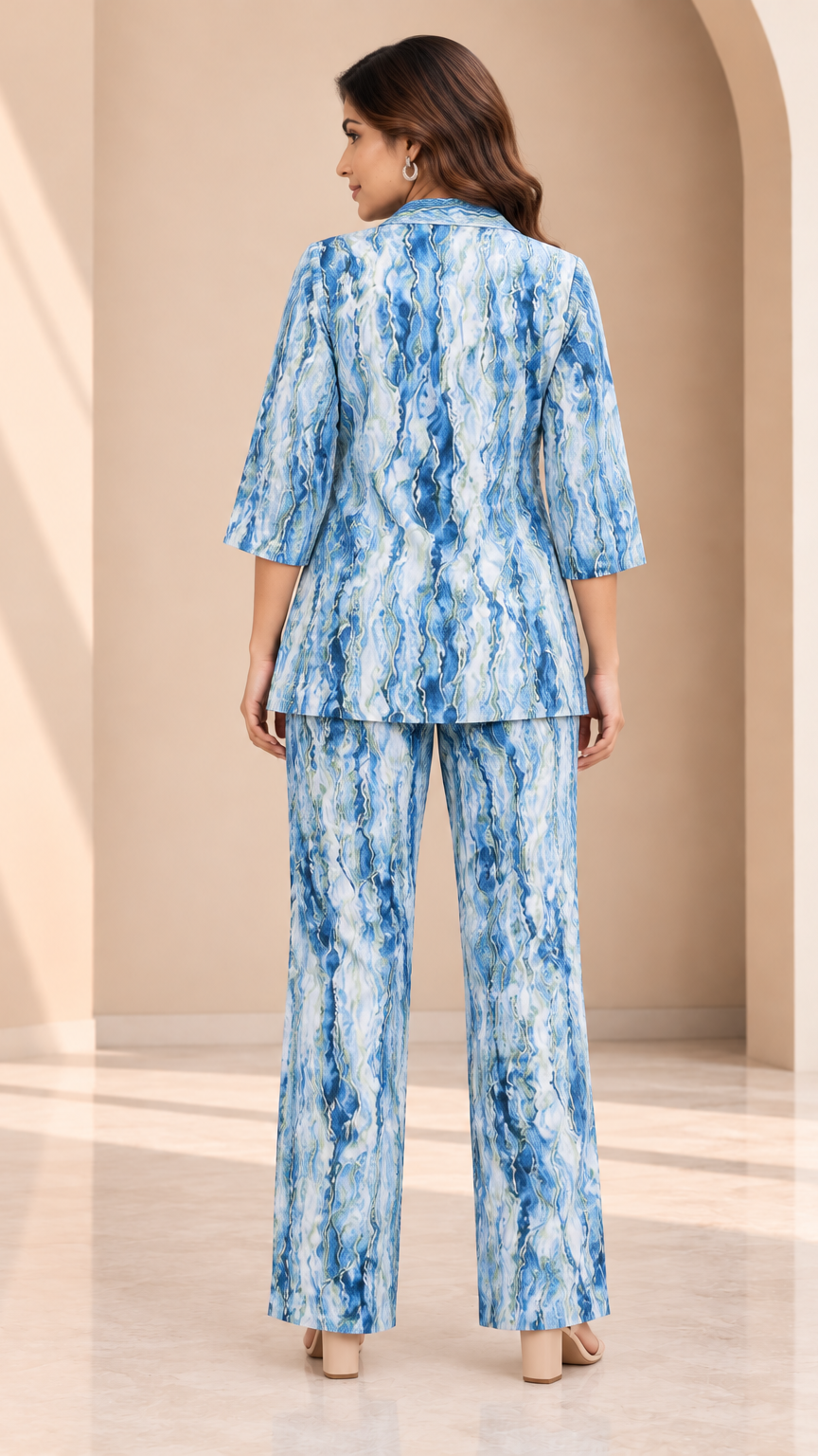A woman viewed from the back wearing a matching blue and white abstract-patterned blazer and wide-leg trousers set, standing in a warm beige architectural interior.