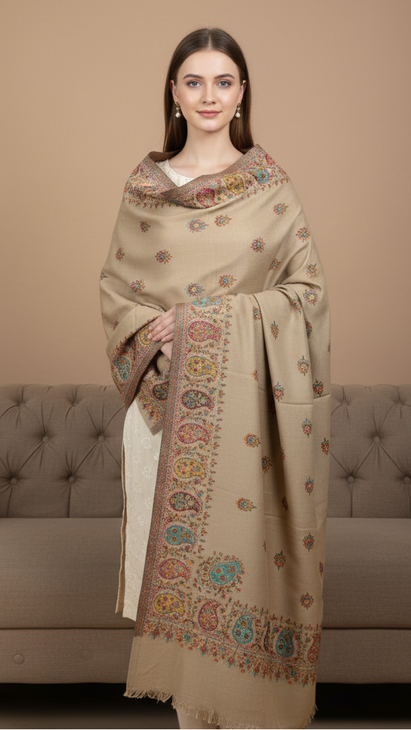 Woman wearing a beige embroidered shawl in front of a beige couch.