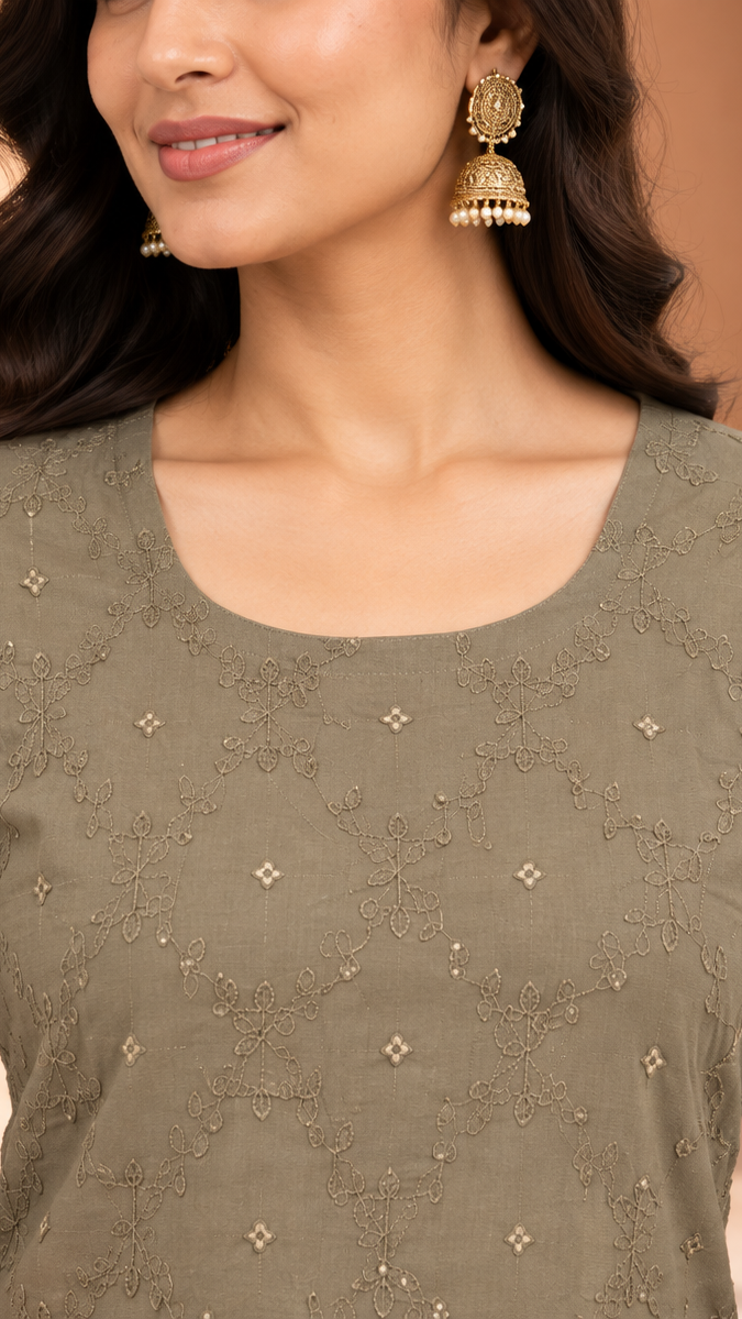 A woman wearing a muted olive green long-sleeve kurta with delicate gold floral embroidery and beadwork, paired with gold jhumka earrings, set against a warm beige background.