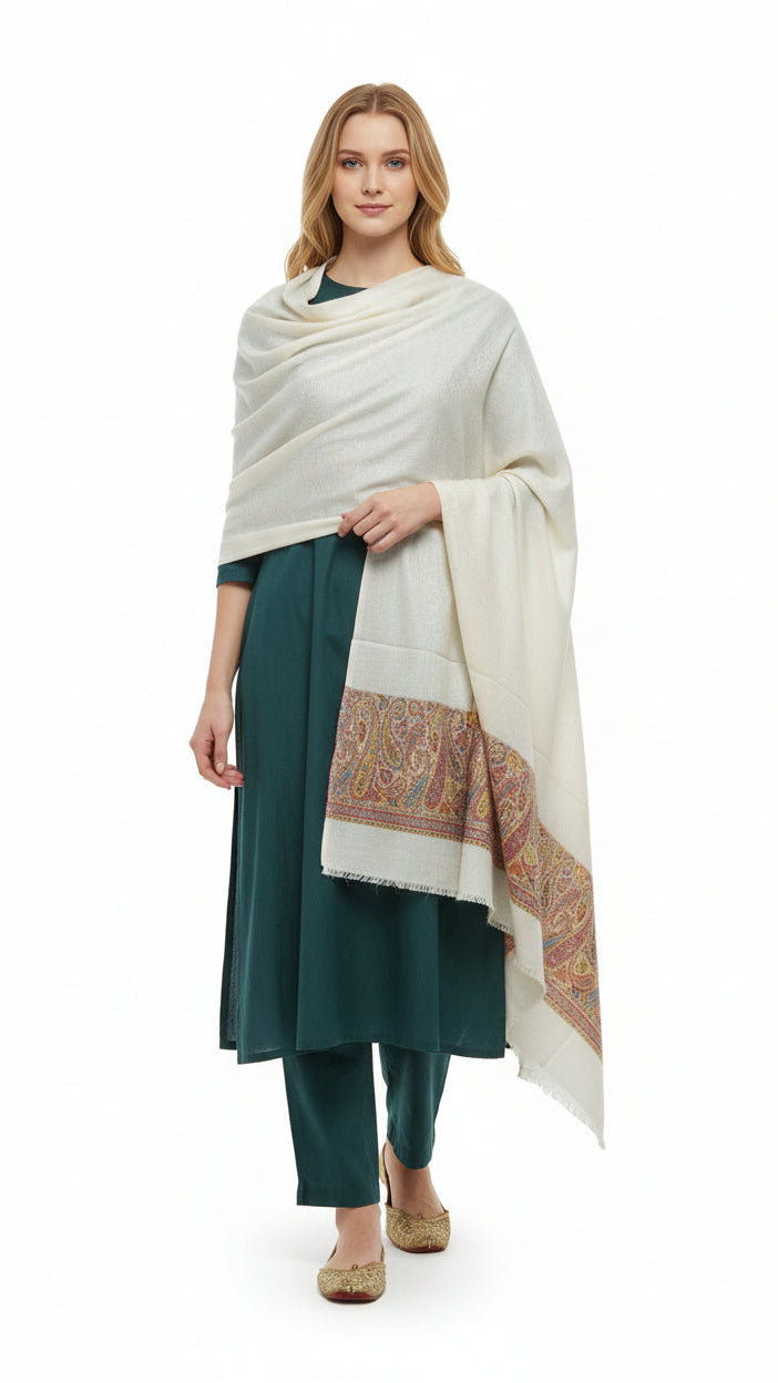 Woman wearing a white shawl with a patterned border over a green outfit on a white background