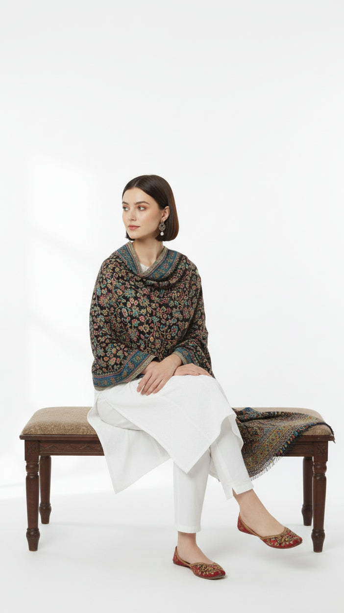 Woman sitting on a bench wearing a patterned sweater and white pants against a white background