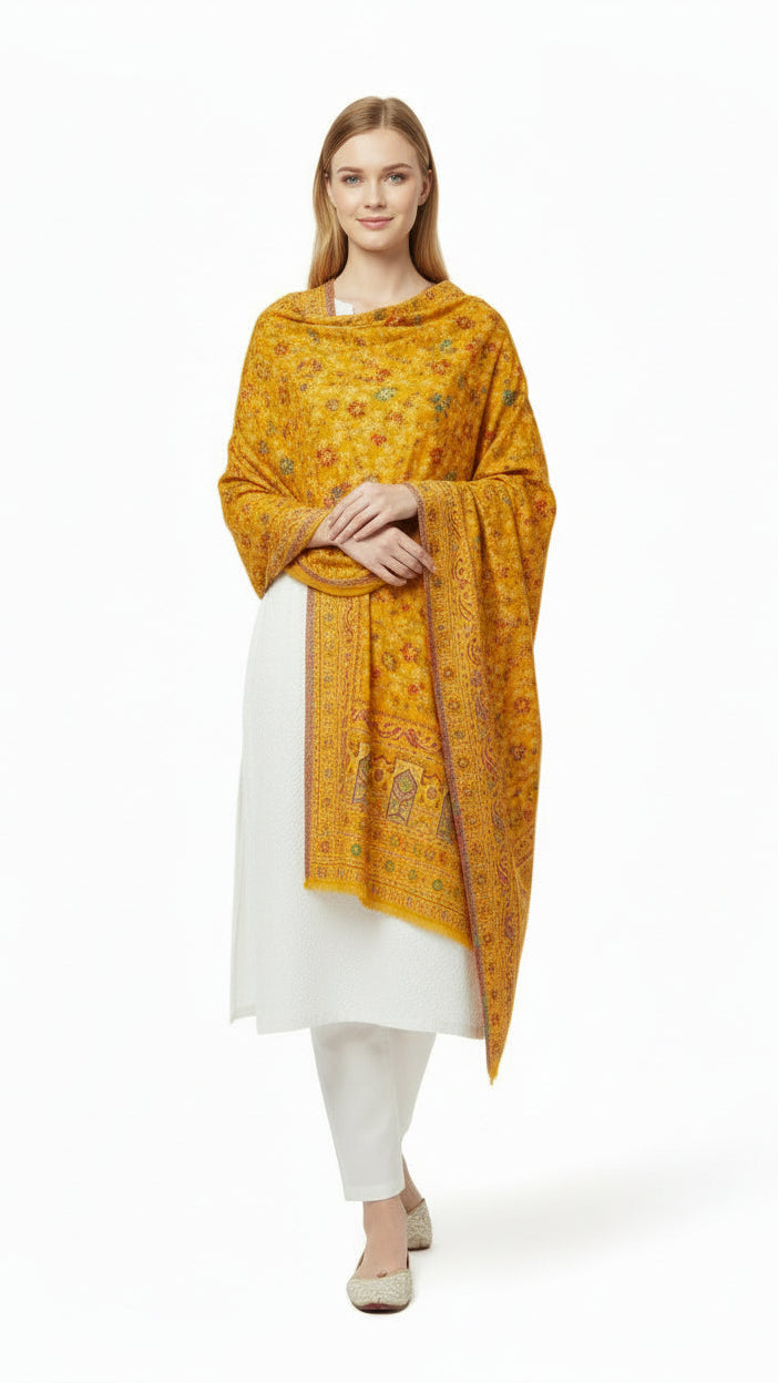 Woman wearing a mustard yellow patterned shawl over a white outfit on a white background