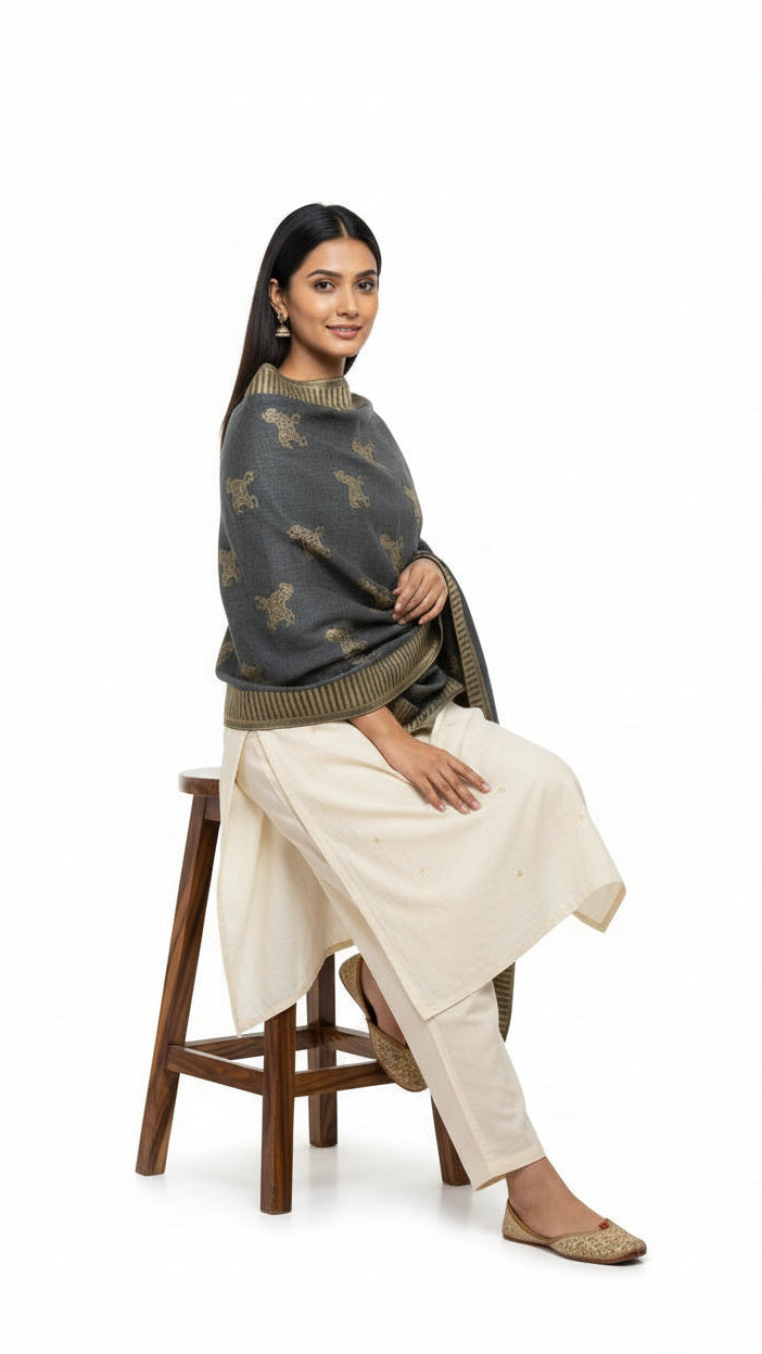 Woman sitting on a stool wearing a dark gray sweater with a pattern and light-colored pants on a white background
