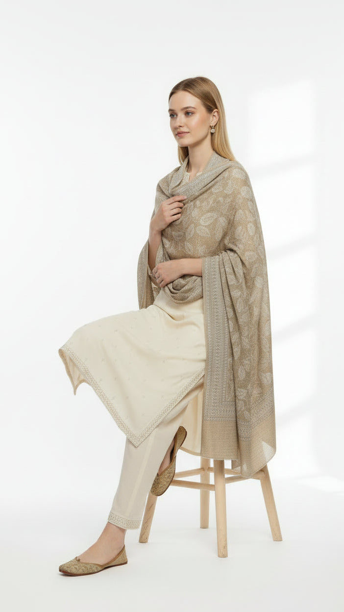 Woman sitting on a stool wearing a beige shawl and dress against a white background
