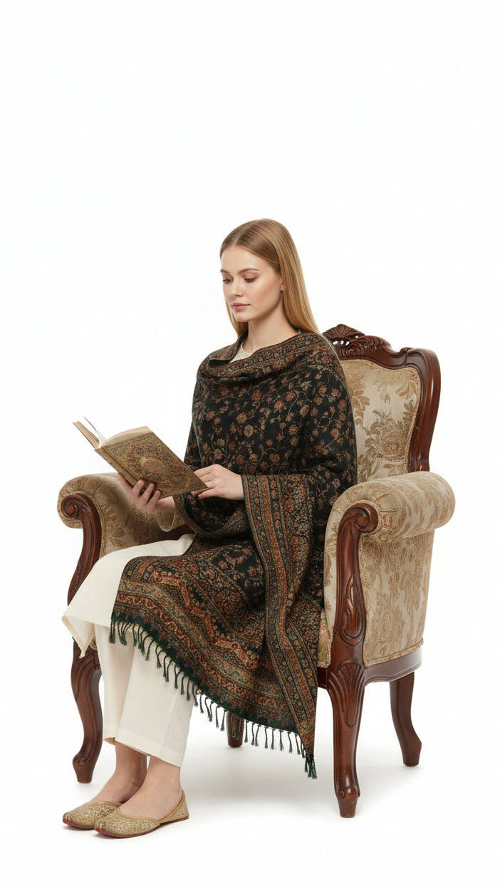 Woman sitting in an ornate armchair wearing a patterned shawl, reading a book.