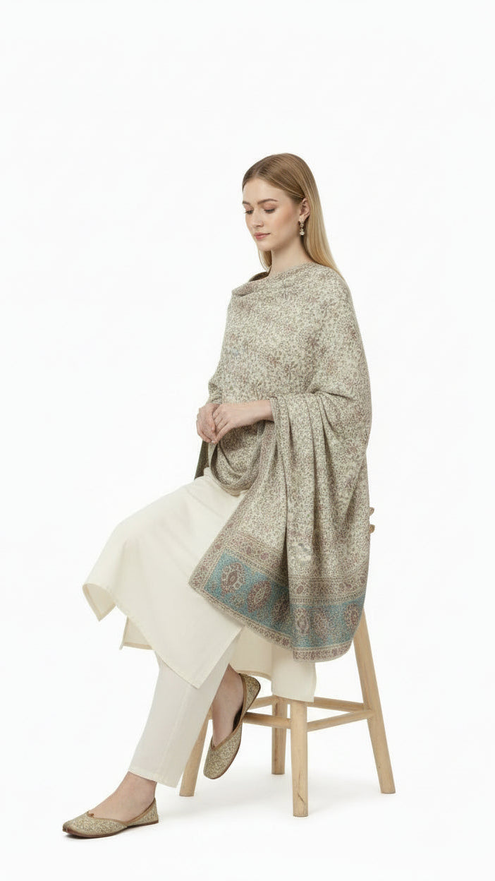 Woman sitting on a stool wearing a patterned shawl over a white outfit on a white background